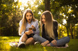 © Sunrise Team - Shocked surprised girls sisters students sitting in the park outdoors on grass using mobile phone listening music with earphones.