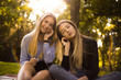 © Sunrise Team - Happy girls sisters students sitting in the park outdoors on grass have a rest listening music with earphones.