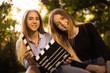 © Sunrise Team - Happy girls sisters students sitting in the park outdoors on grass have a rest holding film making clapperboard.