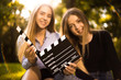 © Sunrise Team - Happy girls sisters students sitting in the park outdoors on grass have a rest holding film making clapperboard. Focus on clapperboard.
