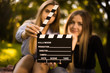 © Sunrise Team - Happy girls sisters students sitting in the park outdoors on grass have a rest holding film making clapperboard. Focus on clapperboard.
