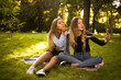 © Sunrise Team - Girls sisters students sitting in the park outdoors on grass have a rest take a selfie by mobile phone blowing kisses.