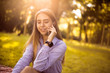 © Sunrise Team - Happy cheerful smiling girl student sitting in the park outdoors on grass have a rest talking by mobile phone.