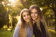 © Sunrise Team - Happy laughing girls sisters students standing in the park outdoors on grass have a rest looking camera hugging.