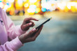 Person pointing finger on screen smartphone on defocus background bokeh light in evening street, hipster girl using in hands mobile phone gadget in night atmospheric city, online wifi internet concept