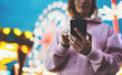 girl pointing finger on screen smartphone on defocus background bokeh light in evening street attraction, woman using in hands mobile phone gadget in night city, online wifi internet concept