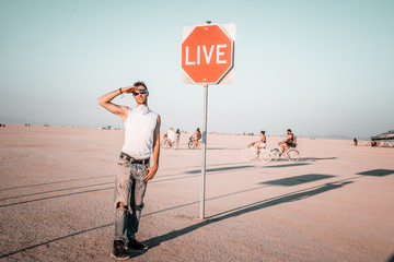 Wall Mural - Young man by the dream and live sign in the middle of a desert. Sign to live your life.