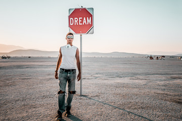 Wall Mural - Young man by the dream and live sign in the middle of a desert. Sign to live your life.