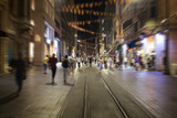 Fototapeta Londyn - Blurry motion image of people walking in Istiklal Avenue (the city’s main pedestrian boulevard) at night in Istanbul. The street which is lined with 19th-century buildings, shopping chains and cafes.