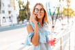 Portrait of a beautiful girl student, wearing glasses, talking on the phone in a good mood, and holding a cocktail