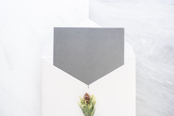 Poster - Top view of blank grey card in white envelop with pine leaf on two layer step of marble table top.Mock up template for display of design.modern business items.