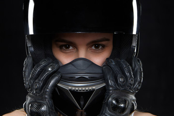 Beautiful young woman in black leather gloves and protective motorbike helmet in studio. Attractive self determined female motocycle racer wearing hands and body protection from falls and accidents