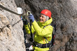 © makasana photo - young  female mountain climber on a Via Ferrata in the Dolomites in Alta Badia clicking carabiners in the cable for safety and smiling