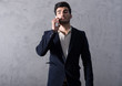 © Spectral-Design - A serious handsome young businessman in a black suit talking on his phone in front of a grey wall in a studio.