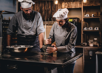 Assistant cook grinds sesame seeds in a mortar for cooking bread. Chef teaching his assistant to bake the bread in the bakery.