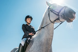 low angle view of attractive female equestrian riding horse against blue sky