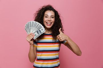 Sticker - Image of young woman 20s with curly hair holding fan of dollar money, isolated over pink background