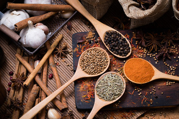 Colorful various spice and herbs in wood spoon on natural texture burned wood plate.