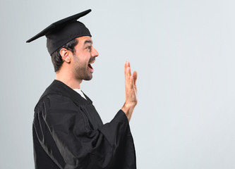 Man on his graduation day University saluting with hand with happy expression on grey background