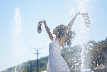 Feeling Of Freedom. Selective Focus Of Fountain Water Drops With Happy Beautiful Woman Standing In The Background