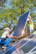 © anatoliy_gleb - Two technicians standing on metal platform adjusting heavy solar photo voltaic panel on bright sunny day. Stand-alone solar panel system installation, efficiency and professionalism concept.