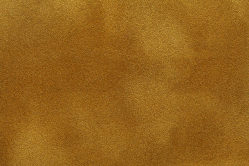 background of dark golden suede fabric closeup. velvet matt texture of yellow nubuck textile