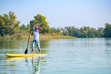  Sporty man paddling on a SUP board on large river
