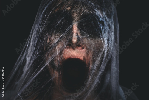 Fotografía Screaming creepy character covered with spiderweb on black background