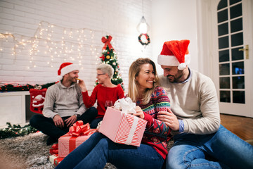 Wall Mural - Young couples celebrating winter holidays together. One couple sitting on side and sharing presents.