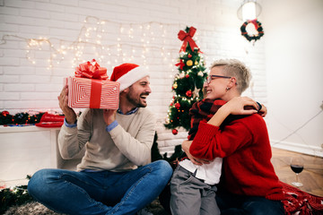 Wall Mural - Happy family on christmas eve sharing presents. Cute little boy hags his mother while father is holding his present.