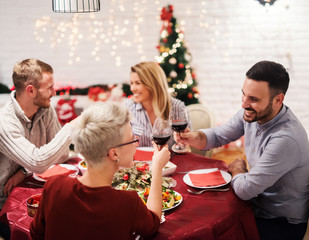 Wall Mural - Two young couples having christmas dinner together. Sitting at decorated table full of food and having fun.