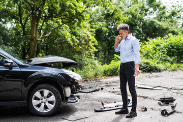 Wall Mural - Mature man standing by the car, making a phone call after a car accident.