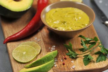 Mexican sauce guacamole. Next to the bowl with sauce, avocado slices, hot red pepper, slices of lime. Close-up. Macro photography. 