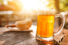 Cold Glass Mug Of Beer With Foam With Bratwurst Hotdog With Sun Beams