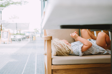 adorable little girl lying on the bench in a cafe outdoors