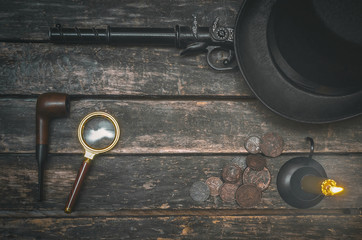 Wall Mural - Musket gun, smoking pipe, magnifying glass, money, bowler hat and burning candle on wooden table background. Detective agent table.