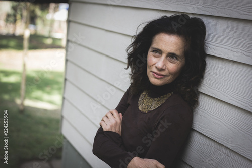 Fotografía Thoughtful mature woman with crossed arms on chest leans on white wood plank wall