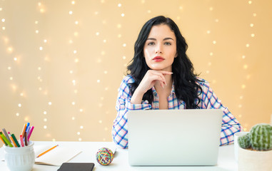 Wall Mural - Young woman with a laptop computer at a desk against an illuminated wall