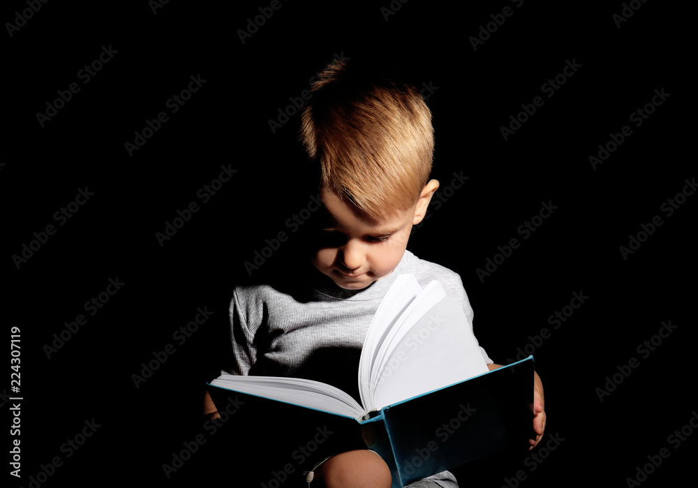 Cute little boy reading book on dark background