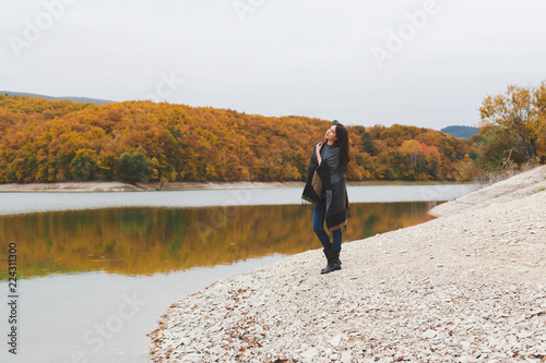 Fotografía Young brunette woman wearing grey poncho standing alone near the lake in autumn