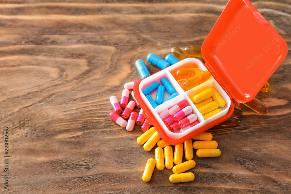 Plastic container with pills on wooden background