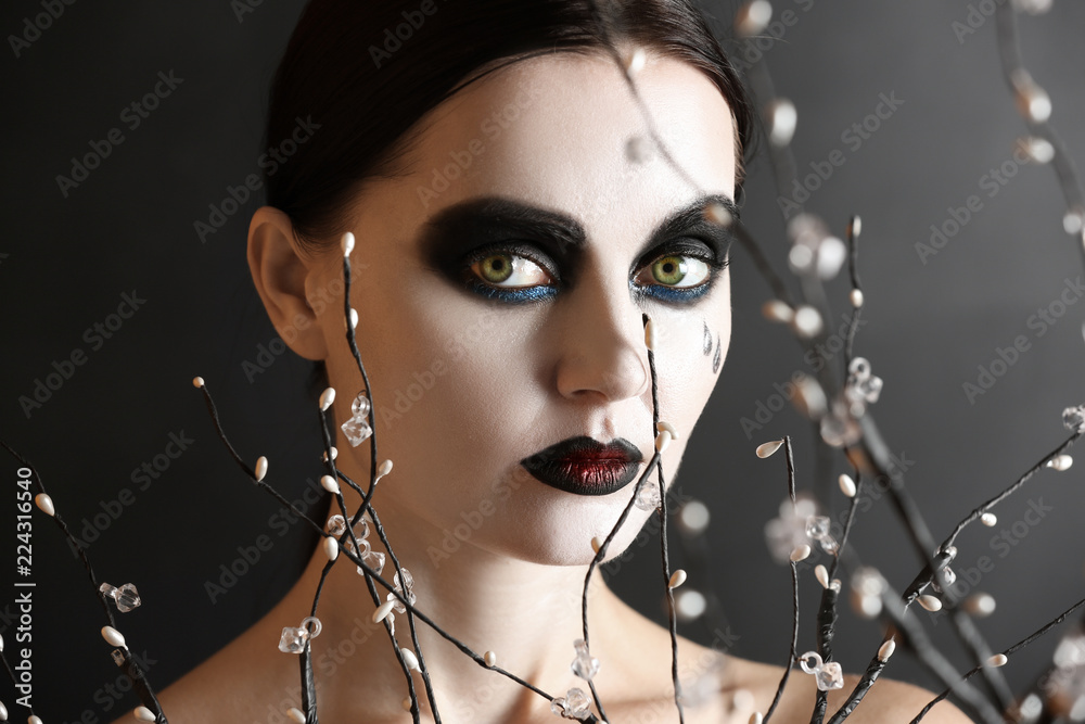 Beautiful woman with Halloween makeup and branches on dark background
