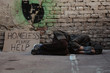 Homeless man lies on the street in the shadow of the old building and begging for help and money. Problems of big modern cities.