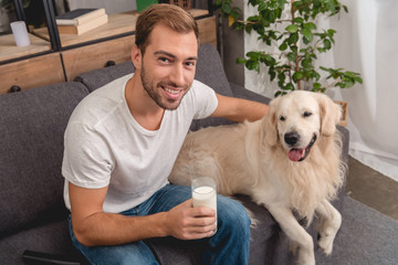 high angle view of smiling young man with glass of milk and adorable golden retriever dog looking at camera