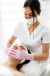 Cosmetologist in  pink gloves  applying cream to the face and massages woman. Cosmetology and professional skin care.Young beautiful dark-haired woman in the office beautician. Close-up
