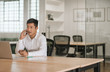 © mavoimages - Young Asian businessman talking on his cellphone in an office