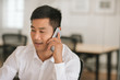 © mavoimages - Smiling Asian businessman talking on a cellphone at work