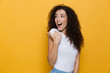 Image of european woman 20s with curly hair pointing finger aside at copyspace, isolated over yellow background