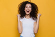 Image of young woman 20s with curly hair yelling and clenching fists, isolated over yellow background