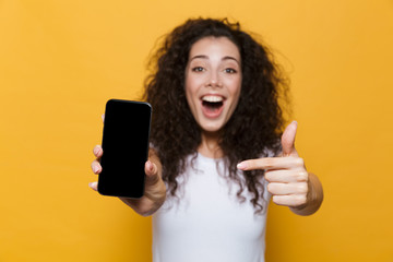 Happy cute young woman posing isolated over yellow background showing display of mobile phone.